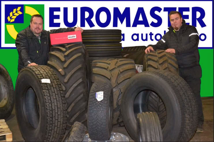 Two people standing among various types of tires with a "Euromaster" sign in the background.
