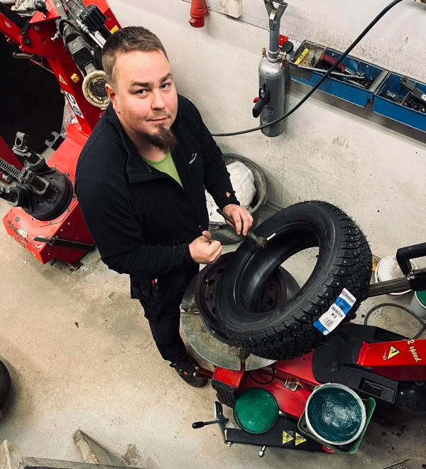 A person standing in a workshop holding a tire, surrounded by tools and equipment.